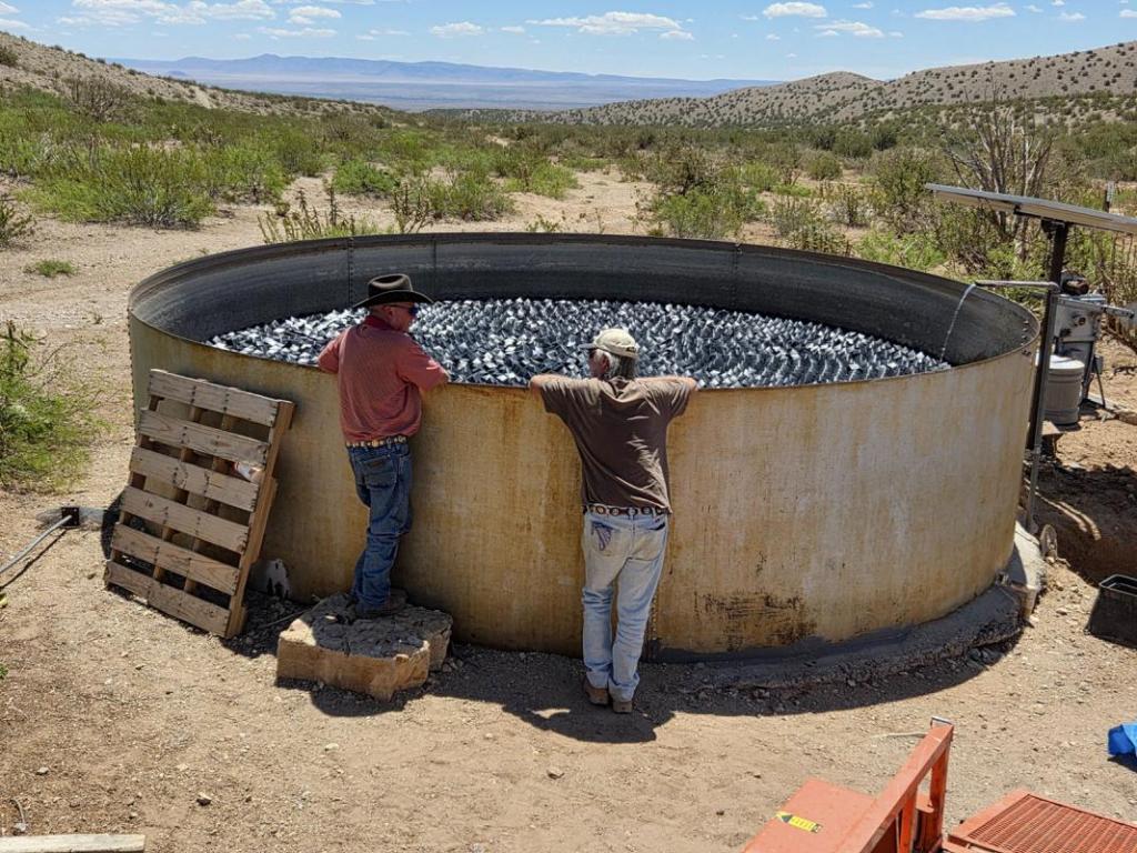 Two men inspect a ranch water tank covered with VaporLok Rhombo shade balls